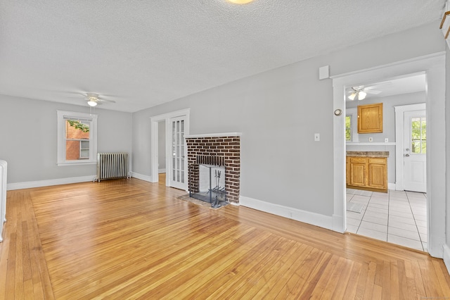 471 New Britain Rd, Berlin, CT 06037 - unfurnished living room with radiator, ceiling fan, a textured ceiling, light wood-type flooring, and a brick fireplace