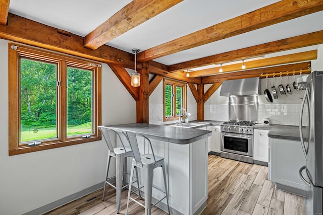 122 Old Post Rd, Old Saybrook, CT 06475 - kitchen with stainless steel appliances, wall chimney range hood, a peninsula, light wood-style floors, and dark countertops