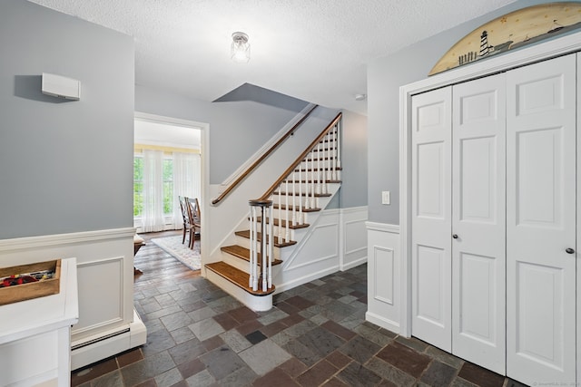 65 Nassahegan Dr, Burlington, CT 06013 - stairs featuring a textured ceiling, a baseboard radiator, stone tile floors, wainscoting, and a decorative wall