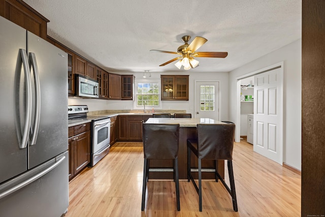 1 Brook Hill Rd, Hamden, CT 06514 - kitchen featuring stainless steel appliances, light wood-style floors, glass insert cabinets, light countertops, and a textured ceiling
