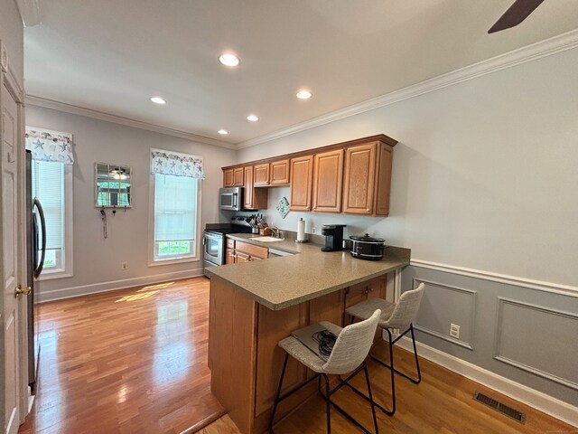 401 Cambridge Commons Unit 401, Middletown, CT 06457 - kitchen featuring stainless steel appliances, crown molding, a kitchen bar, light wood finished floors, and healthy amount of natural light