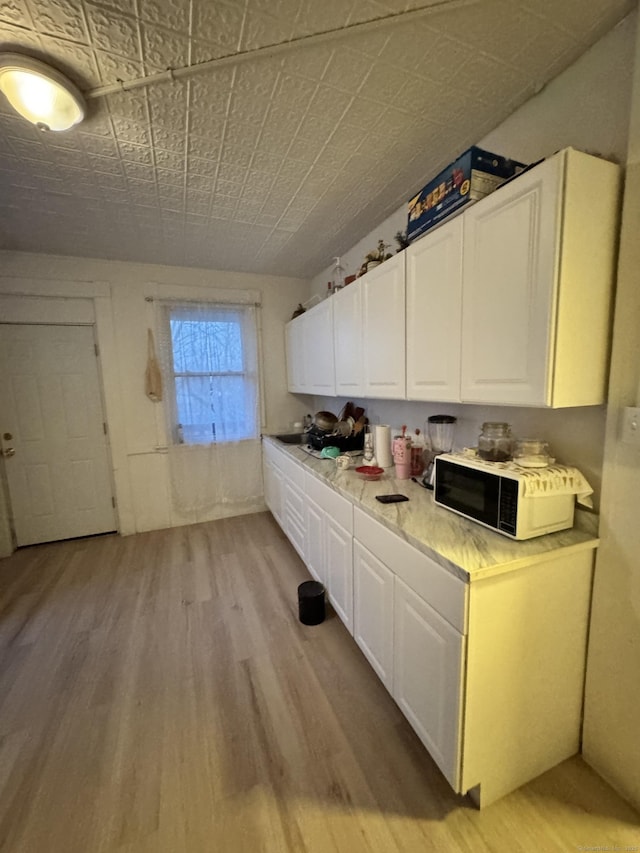 203 S Leonard St, Waterbury, CT 06708 - kitchen with light wood-type flooring, white cabinetry, light countertops, and black microwave