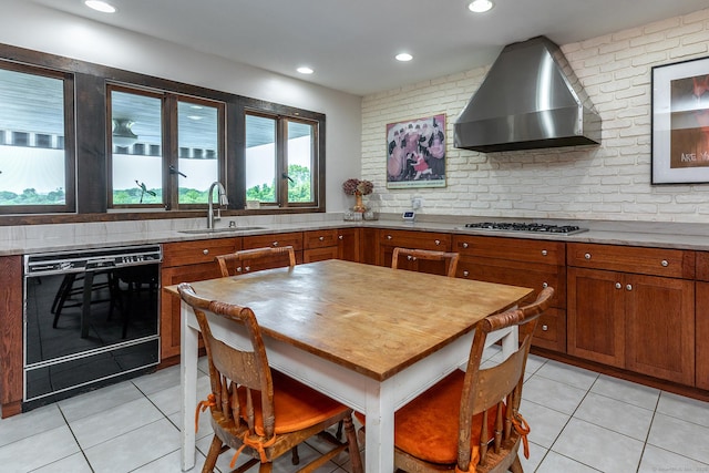 kitchen with black dishwasher, wall chimney exhaust hood, light tile patterned floors, brown cabinetry, and tasteful backsplash