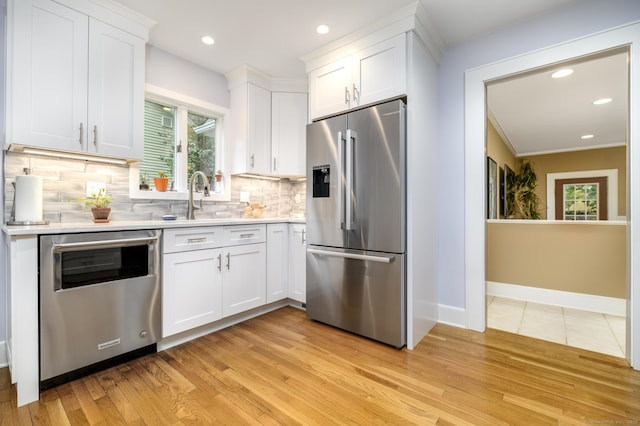 116 Knapp St, Stamford, CT 06907 - kitchen featuring appliances with stainless steel finishes, light countertops, white cabinets, backsplash, and light wood-type flooring
