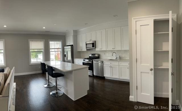 4 Armonk St, Greenwich, CT 06830 - kitchen featuring appliances with stainless steel finishes, a kitchen bar, white cabinetry, dark wood-style floors, and crown molding