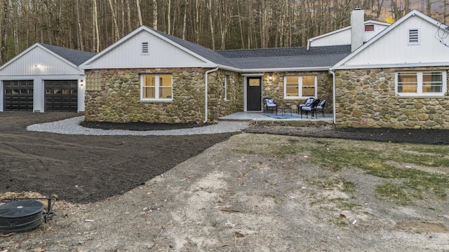 45 Westledge Rd, Simsbury, CT 06092 - view of front of home with stone siding, roof with shingles, a garage, a chimney, and a patio