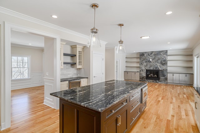 19 Ives Ct, Ridgefield, CT 06877 - kitchen featuring light wood finished floors, a multi sided fireplace, decorative light fixtures, crown molding, and glass insert cabinets