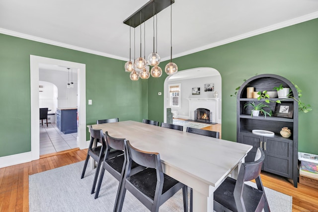 946 Wilcoxson Ave, Stratford, CT 06614 - dining space featuring ornamental molding, arched walkways, light wood-style flooring, a lit fireplace, and a chandelier