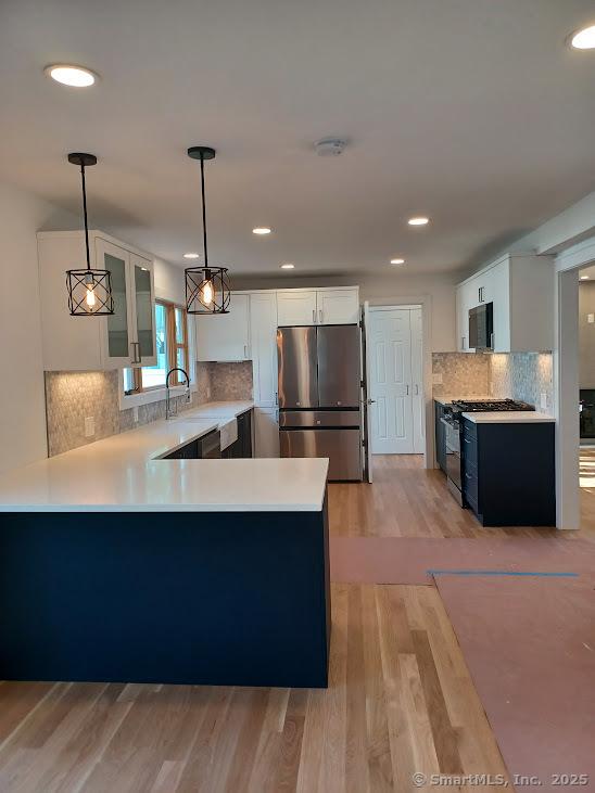 105 Houston Ter, Stamford, CT 06902 - kitchen featuring black appliances, a peninsula, light wood-type flooring, light countertops, and glass insert cabinets