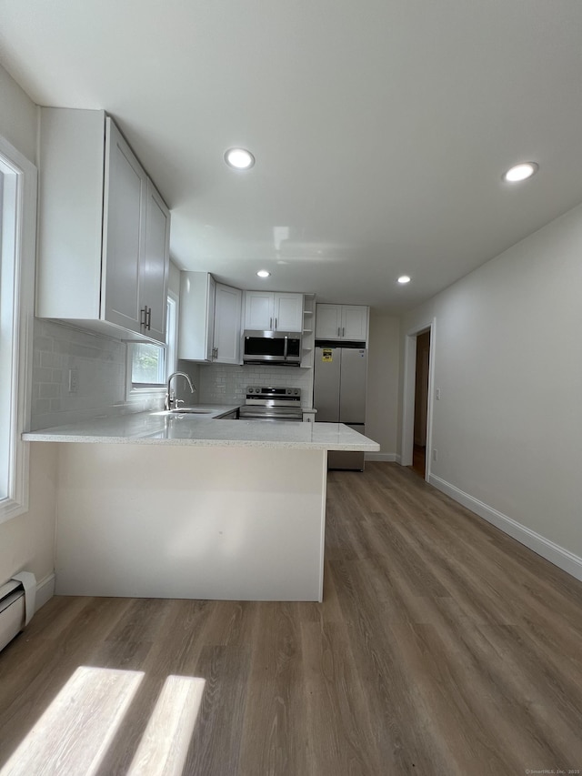 52 Sylvan St, Avon, CT 06001 - kitchen with appliances with stainless steel finishes, a peninsula, wood finished floors, decorative backsplash, and light countertops