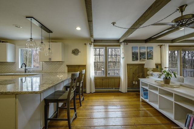127 Skunk Misery Rd, Haddam, CT 06441 - kitchen featuring beam ceiling, white cabinetry, light stone countertops, backsplash, and wainscoting