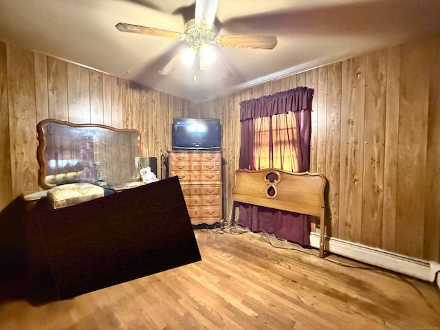 bedroom with wood finished floors, wooden walls, a baseboard heating unit, and ceiling fan