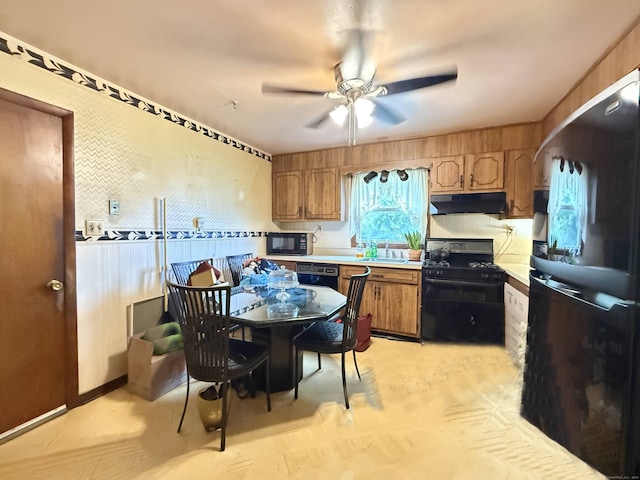 kitchen featuring black appliances, under cabinet range hood, a ceiling fan, light countertops, and brown cabinetry