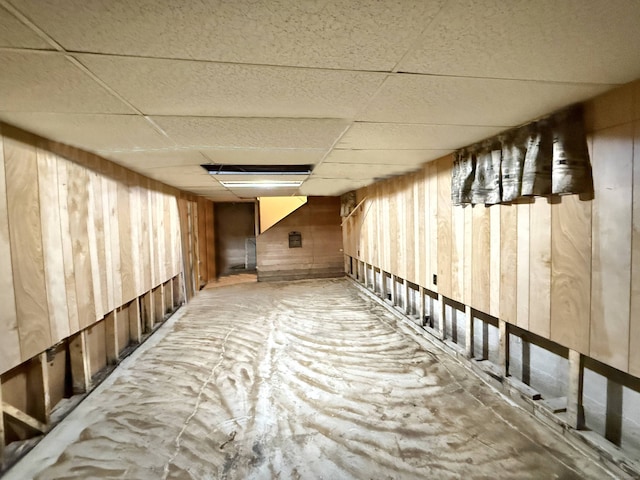 unfinished below grade area with wood walls and a paneled ceiling