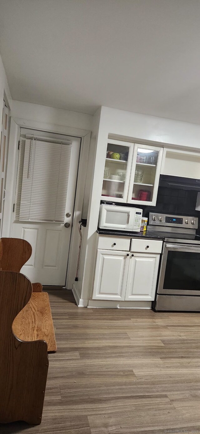 kitchen featuring stainless steel electric stove, white microwave, light wood finished floors, white cabinetry, and dark countertops