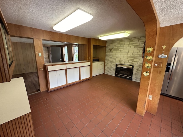 306 Divinity St, Bristol, CT 06010 - unfurnished living room featuring a textured ceiling, wood walls, a stone fireplace, washer / clothes dryer, and dark tile patterned flooring