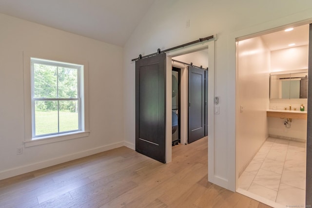 376 Rte 165, Preston, CT 06365 - unfurnished bedroom featuring a barn door, multiple windows, lofted ceiling, connected bathroom, and light wood-style flooring