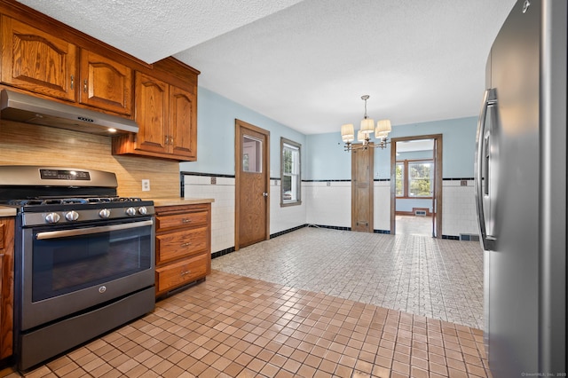 32 Franklin St, Southington, CT 06479 - kitchen with appliances with stainless steel finishes, under cabinet range hood, wainscoting, a chandelier, and tile walls