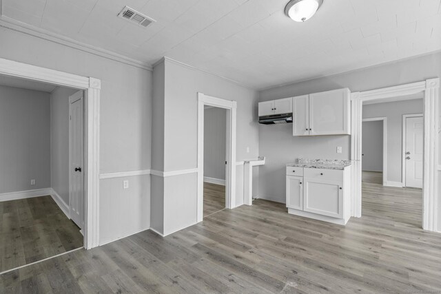 37 William St, Waterbury, CT 06702 - kitchen with white cabinets, under cabinet range hood, light wood-style floors, light countertops, and ornamental molding