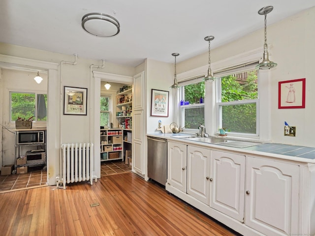58 Riverdale Ave, Greenwich, CT 06831 - kitchen with radiator heating unit, appliances with stainless steel finishes, white cabinets, light wood finished floors, and decorative light fixtures