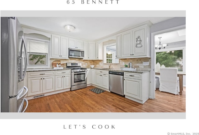 65 Bennett St, Fairfield, CT 06825 - kitchen with stainless steel appliances, a chandelier, decorative backsplash, white cabinetry, and light wood-style floors