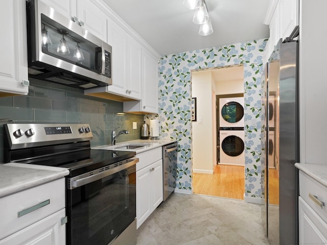 155 Brewster St Apt 3K, Bridgeport, CT 06605 - kitchen featuring wallpapered walls, appliances with stainless steel finishes, estacked washer and dryer, white cabinetry, and light countertops