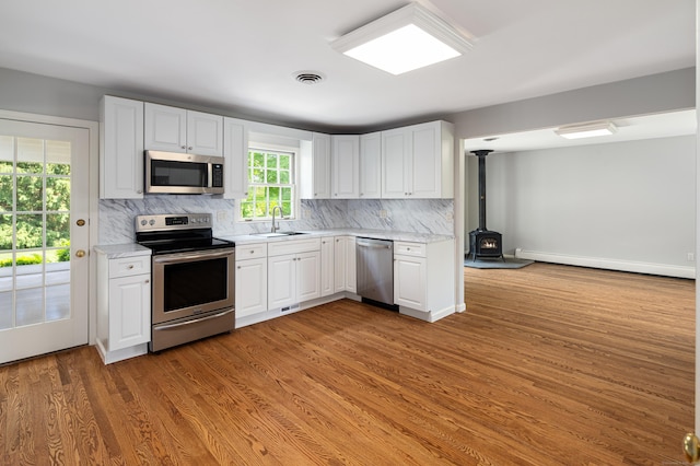 173 Russet Rd, Stamford, CT 06903 - kitchen featuring appliances with stainless steel finishes, a baseboard radiator, a wood stove, tasteful backsplash, and white cabinetry