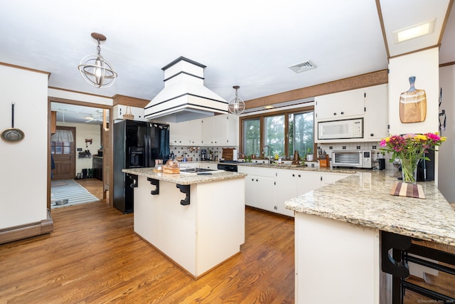 123 Silkey Rd, Granby, CT 06060 - kitchen featuring black fridge with ice dispenser, white microwave, white cabinetry, a breakfast bar, and a peninsula