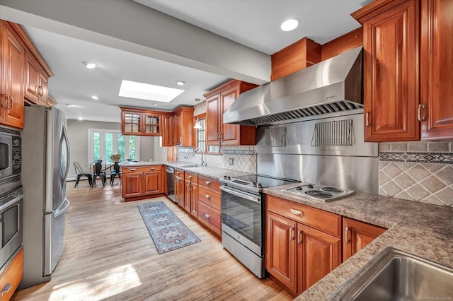 421 Hemlock Point Dr, Coventry, CT 06238 - kitchen with wall chimney exhaust hood, appliances with stainless steel finishes, brown cabinetry, light wood-style floors, and a skylight