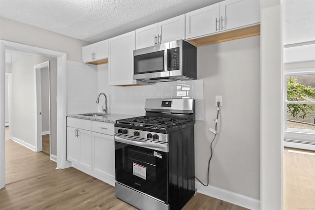 96 Naugatuck Ave, Milford, CT 06460 - kitchen with appliances with stainless steel finishes, light wood-type flooring, backsplash, white cabinets, and a textured ceiling