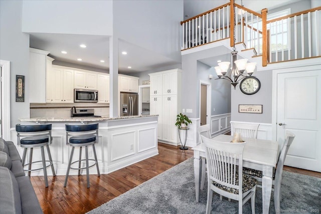 17 Brookside Ct Unit 17, Newtown, CT 06470 - dining space featuring a high ceiling, dark wood-style flooring, a chandelier, wainscoting, and a decorative wall