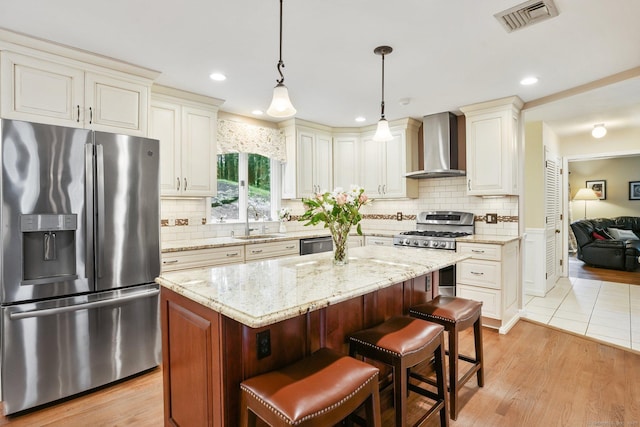 58 Inca Dr, Trumbull, CT 06611 - kitchen featuring stainless steel appliances, wall chimney exhaust hood, a kitchen island, light stone counters, and light wood-type flooring
