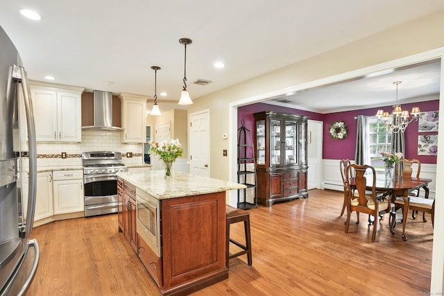 58 Inca Dr, Trumbull, CT 06611 - kitchen with appliances with stainless steel finishes, wall chimney range hood, a kitchen bar, light stone countertops, and light wood finished floors