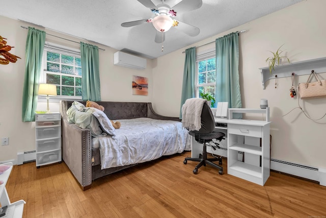 81 Charter Oak Dr, East Lyme, CT 06333 - bedroom with a wall mounted air conditioner, light wood-style flooring, a baseboard radiator, ceiling fan, and a textured ceiling