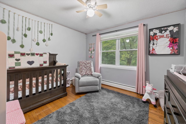 489 Thomaston Rd, Watertown, CT 06795 - bedroom with baseboard heating, wood finished floors, a crib, ceiling fan, and a textured ceiling
