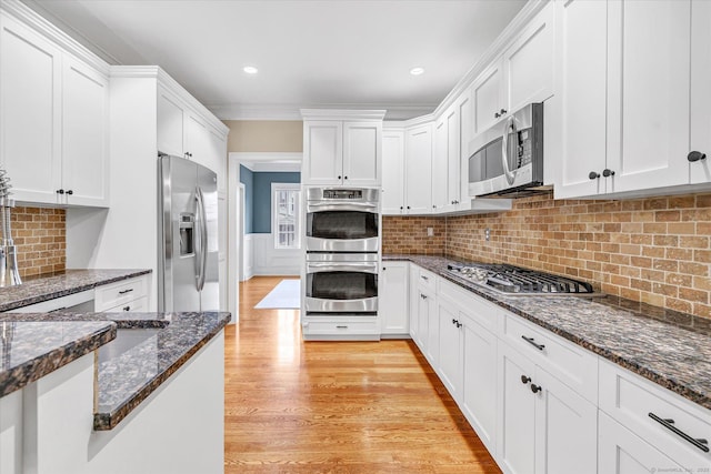 27 Bartlett Ln Unit 27, Shelton, CT 06484 - kitchen with appliances with stainless steel finishes, white cabinetry, dark stone countertops, light wood-style flooring, and tasteful backsplash