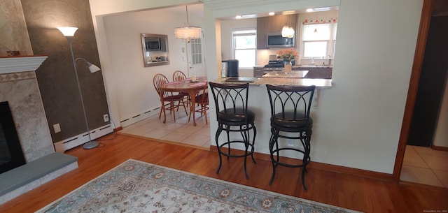 92 Sumac St, West Haven, CT 06516 - kitchen featuring stainless steel microwave, wood finished floors, a breakfast bar area, baseboard heating, and decorative light fixtures