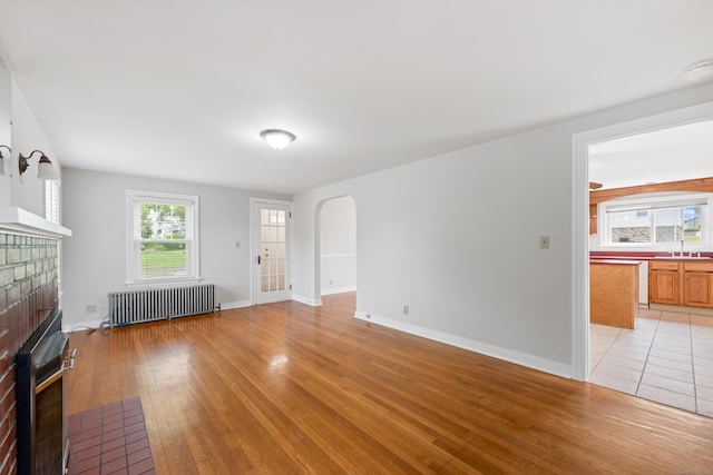 630 French St, Watertown, CT 06779 - unfurnished living room featuring radiator heating unit, a brick fireplace, arched walkways, and light wood-type flooring