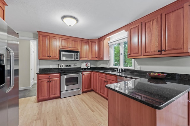 30 Clifdon Dr, Simsbury, CT 06070 - kitchen featuring appliances with stainless steel finishes, brown cabinetry, light wood-style flooring, dark stone countertops, and a peninsula