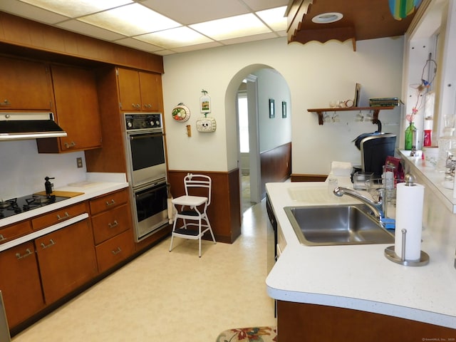 58 Edward St, East Haven, CT 06512 - kitchen featuring black appliances, ventilation hood, arched walkways, brown cabinetry, and wainscoting
