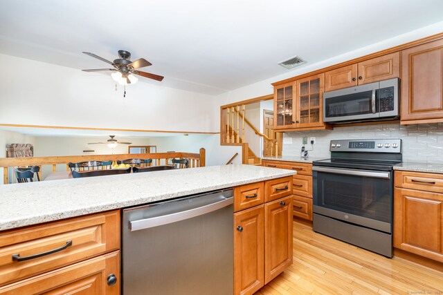 6 Old Sawmill Dr, Beacon Falls, CT 06403 - kitchen featuring appliances with stainless steel finishes, ceiling fan, light wood-style flooring, tasteful backsplash, and glass insert cabinets