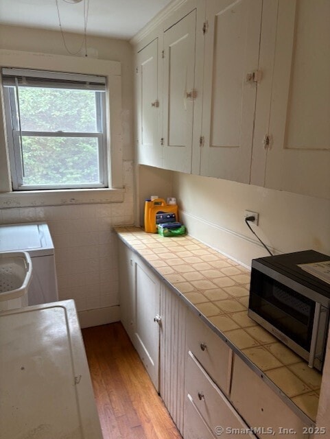 31 Happy St, Norwich, CT 06360 - kitchen featuring stainless steel microwave, tile counters, light wood finished floors, washing machine and clothes dryer, and white cabinets