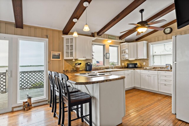 kitchen with freestanding refrigerator, black microwave, a peninsula, backsplash, and glass insert cabinets