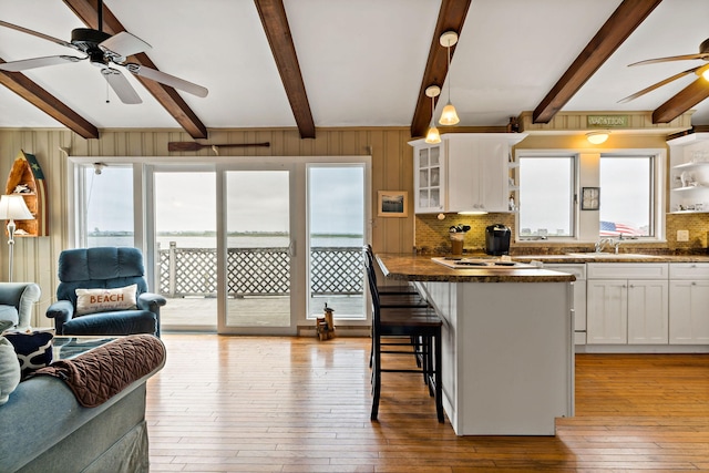 kitchen with ceiling fan, decorative backsplash, beamed ceiling, light wood-style flooring, and white cabinetry