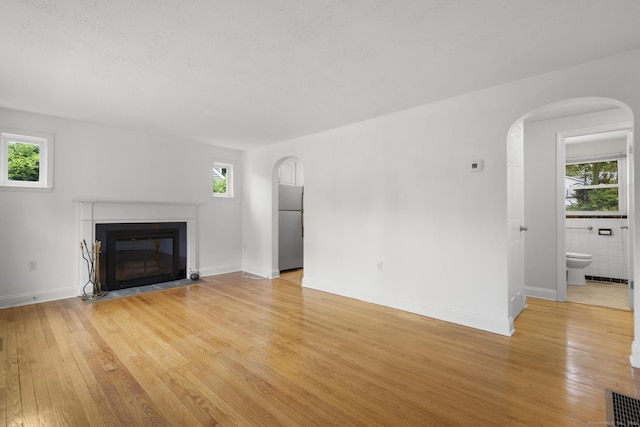 80 Holly St, Milford, CT 06460 - unfurnished living room featuring arched walkways, light wood finished floors, and a fireplace with flush hearth