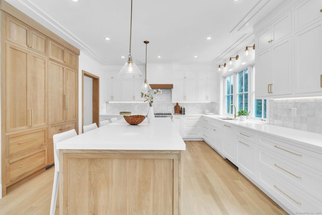 133 E Ave Unit A, New Canaan, CT 06840 - kitchen featuring light wood-type flooring, light countertops, a kitchen island, decorative backsplash, and white cabinetry