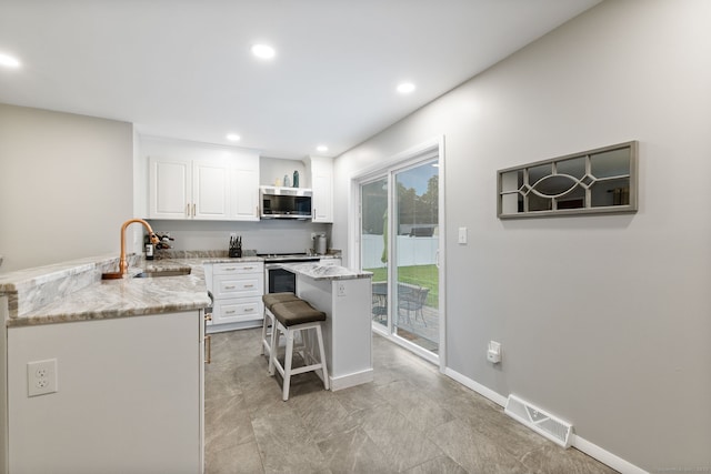 301 Pondview Dr, Southington, CT 06489 - kitchen featuring appliances with stainless steel finishes, white cabinetry, a kitchen bar, light stone countertops, and recessed lighting