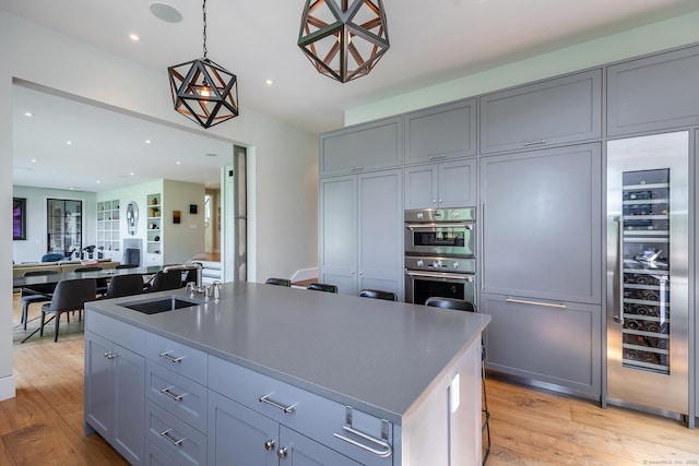 85 W Church Hill Rd, Washington, CT 06794 - kitchen featuring gray cabinetry, light wood-style flooring, a center island with sink, stainless steel double oven, and hanging light fixtures