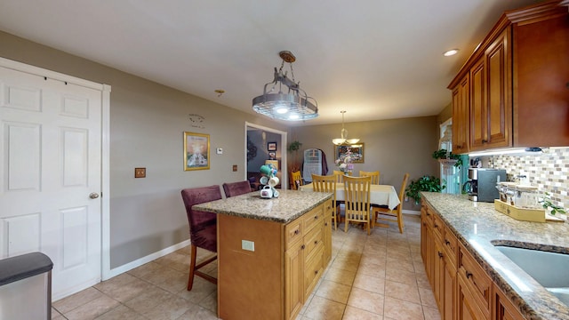 345 Goodwin St, East Hartford, CT 06108 - kitchen with a breakfast bar, light stone counters, a chandelier, decorative backsplash, and brown cabinets