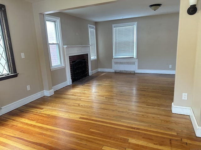 27 Woodbridge Ave, East Hartford, CT 06108 - unfurnished living room with radiator, light wood-style flooring, a fireplace, and plenty of natural light